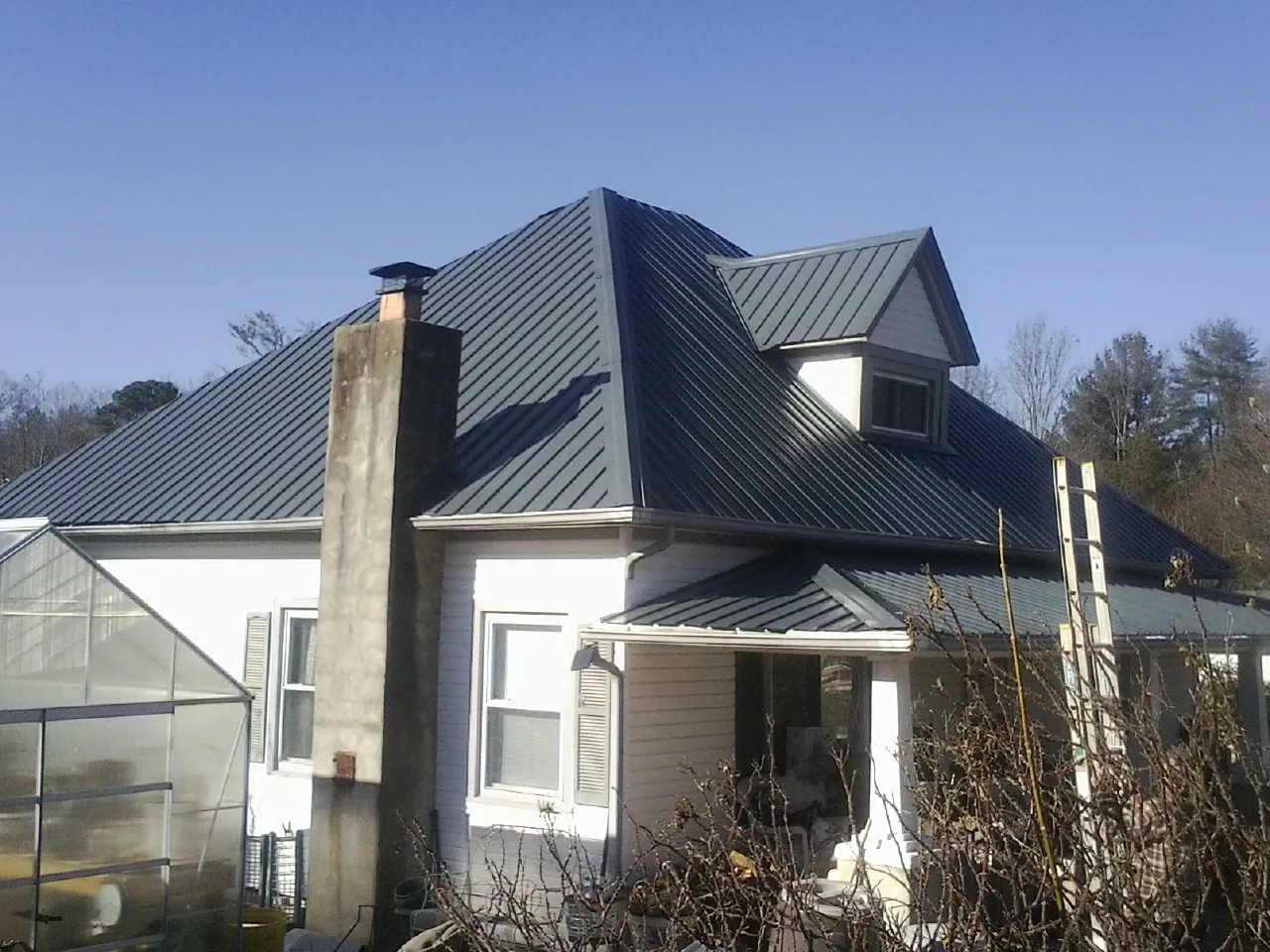 Dark blue standing seam metal roof on a white farmhouse with dormer — Slate & Tile Roof Repair by Roofing Brothers in Sumner