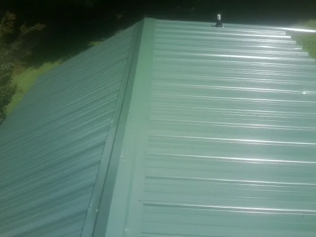 New green metal panels meeting at the ridge of a roof — Flat Roof Repair work by our crew in Sumner