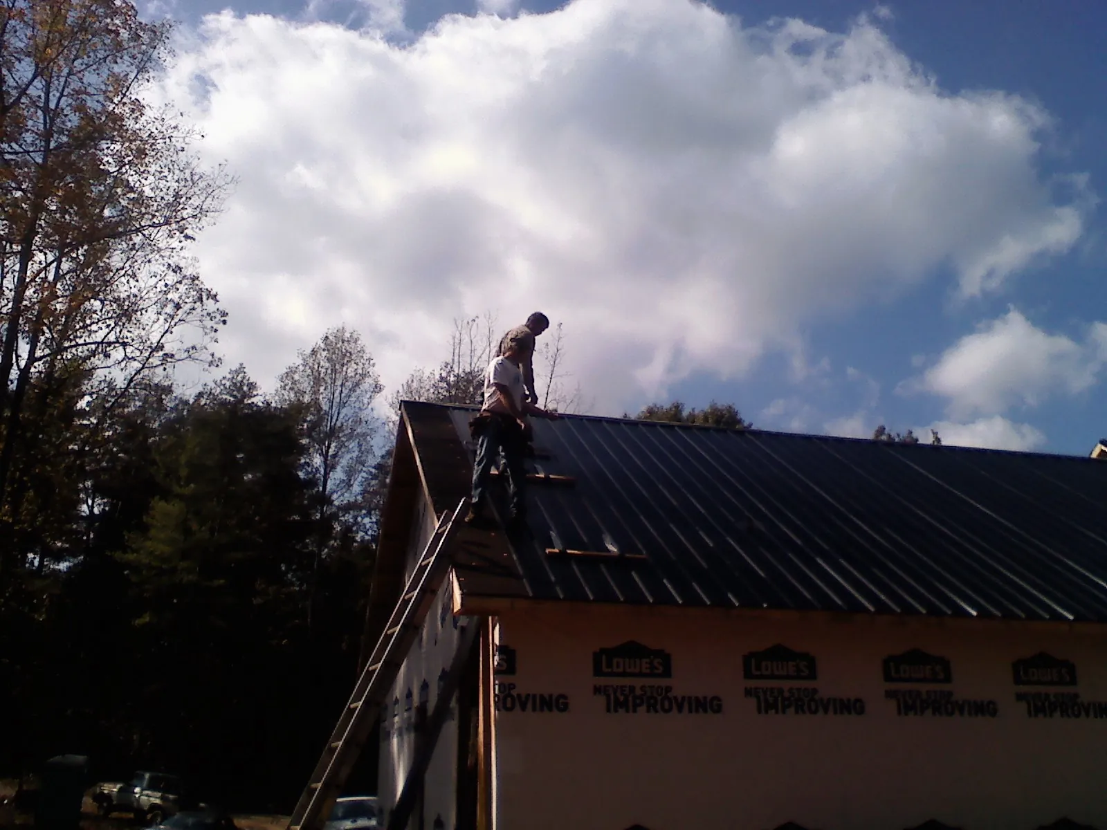 Roofer fastening dark metal panels high against a cloudy sky, from a Roof Inspection job in Sumner